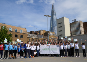 Crowd of children and young people posting with the Marlborough Sports Garden flag together with coaches and the Shard is visible in the background